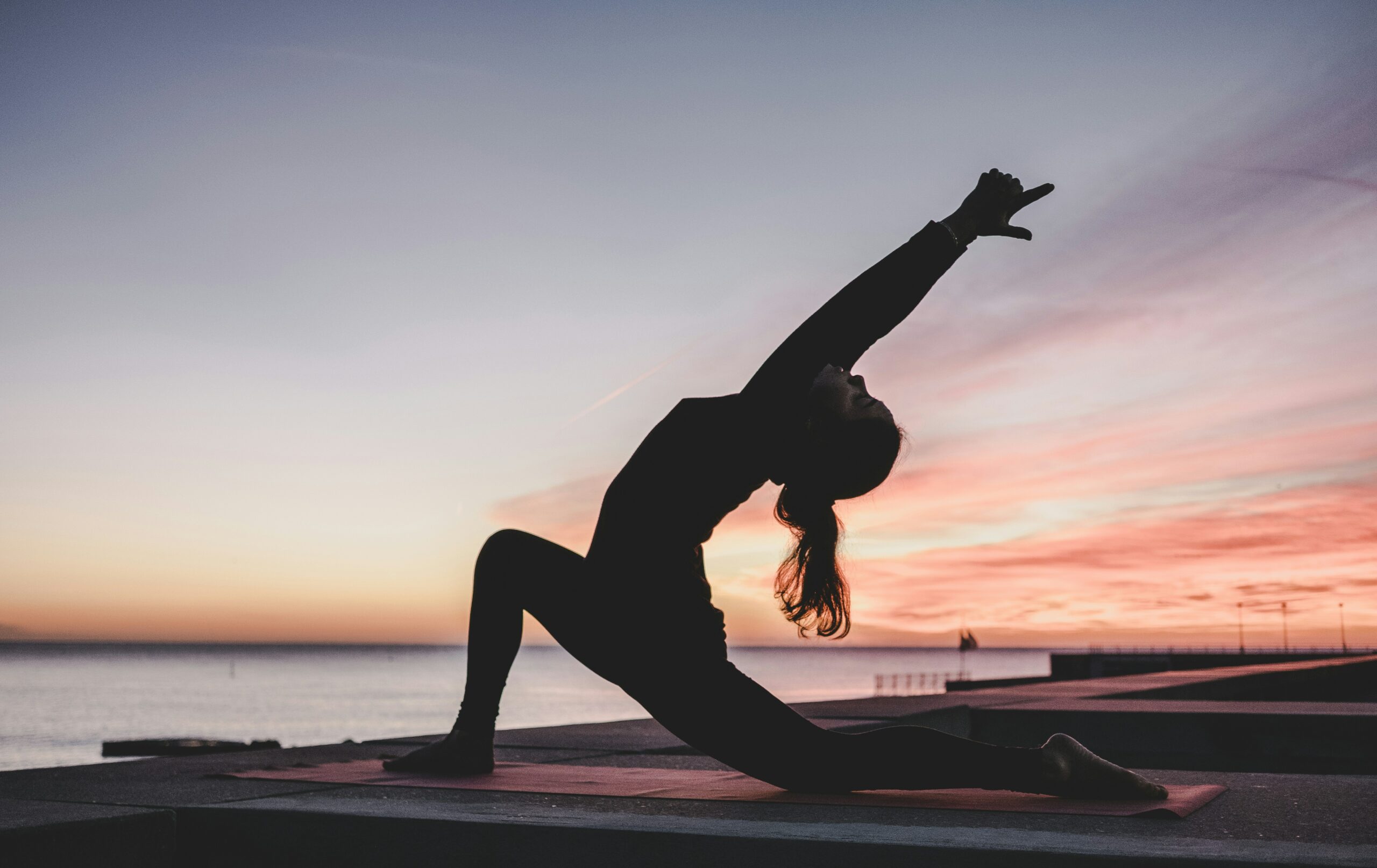 Woman doing sunrise yoga by the water to support a productive and mindful morning routine